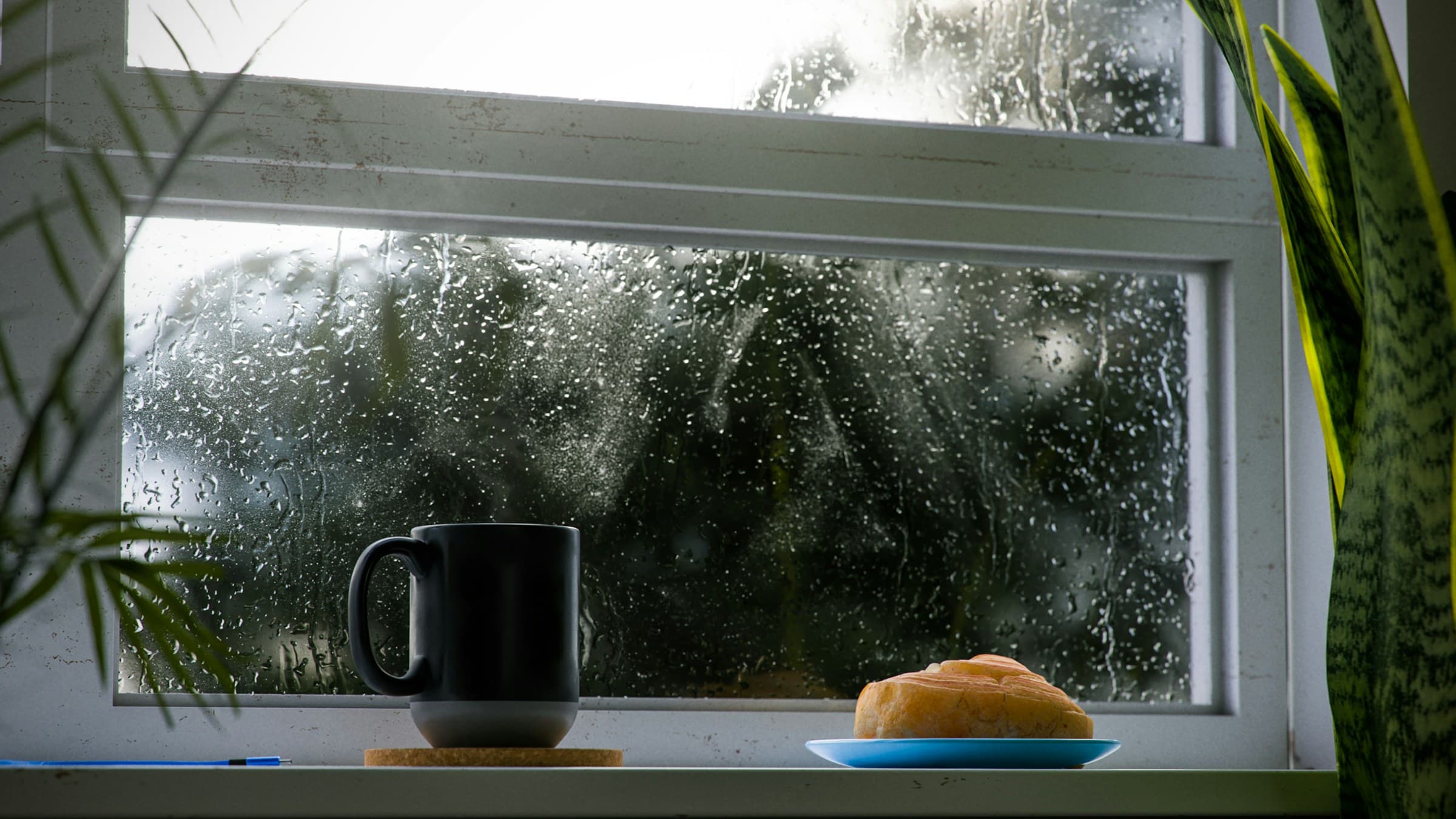 Tasse de café et morceau de pain posés sur le rebord d'une fenêtre par temps gris